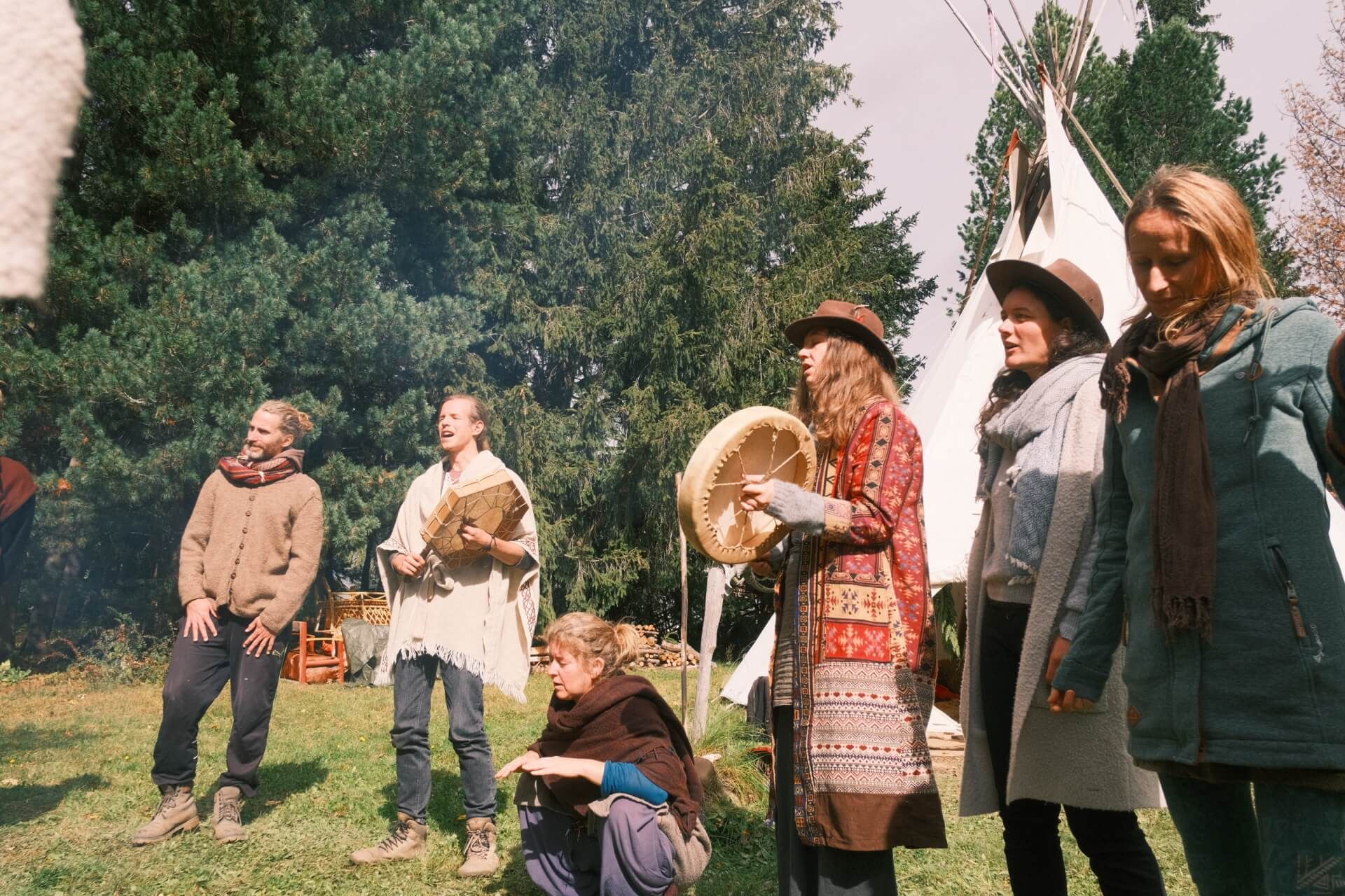Gruppe mit Rahmentrommel vor weißen Tipis auf einer Wiese