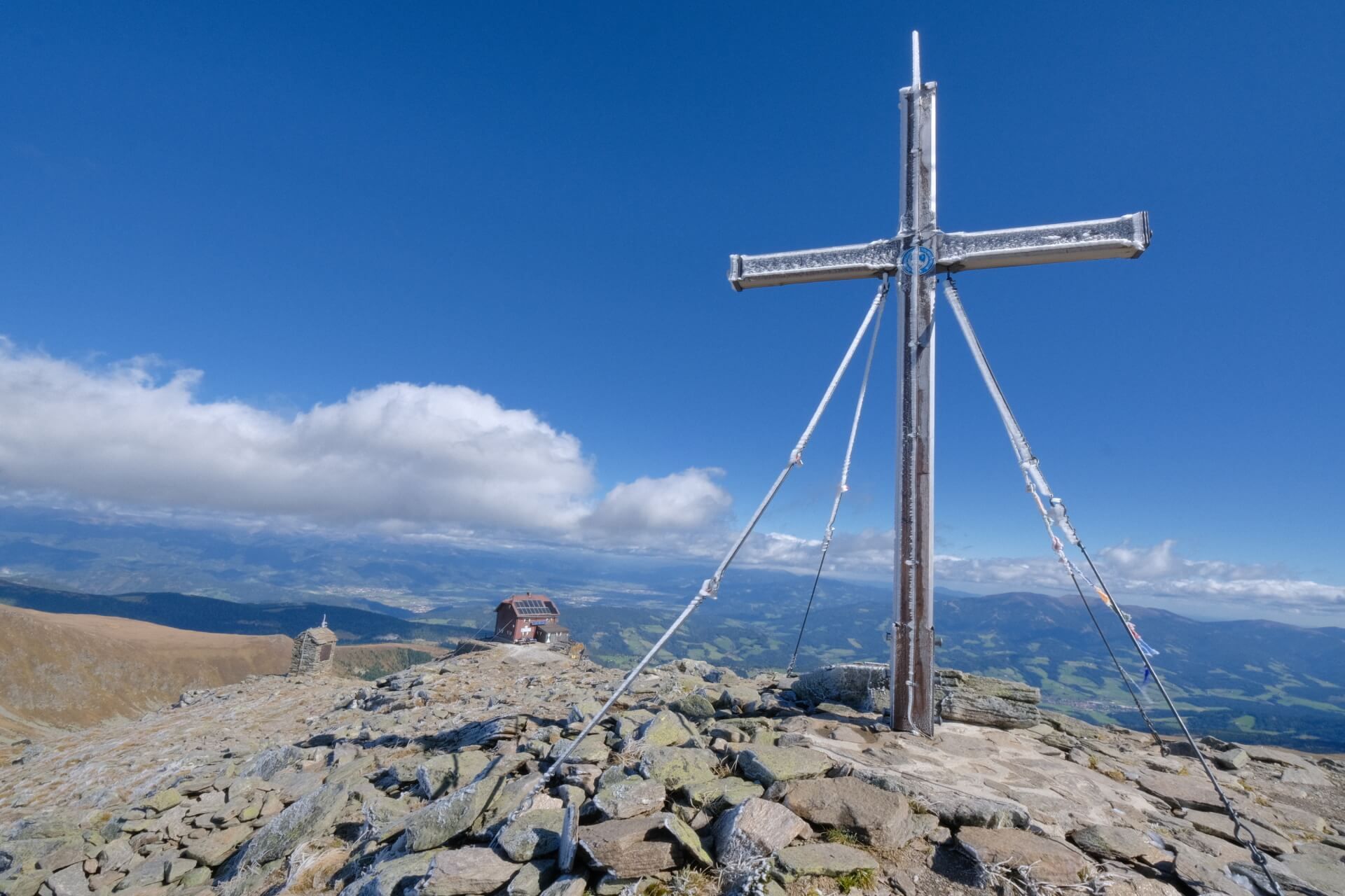 Gipfelkreuz auf einem steinigen Gipfel unter blauem Himmel