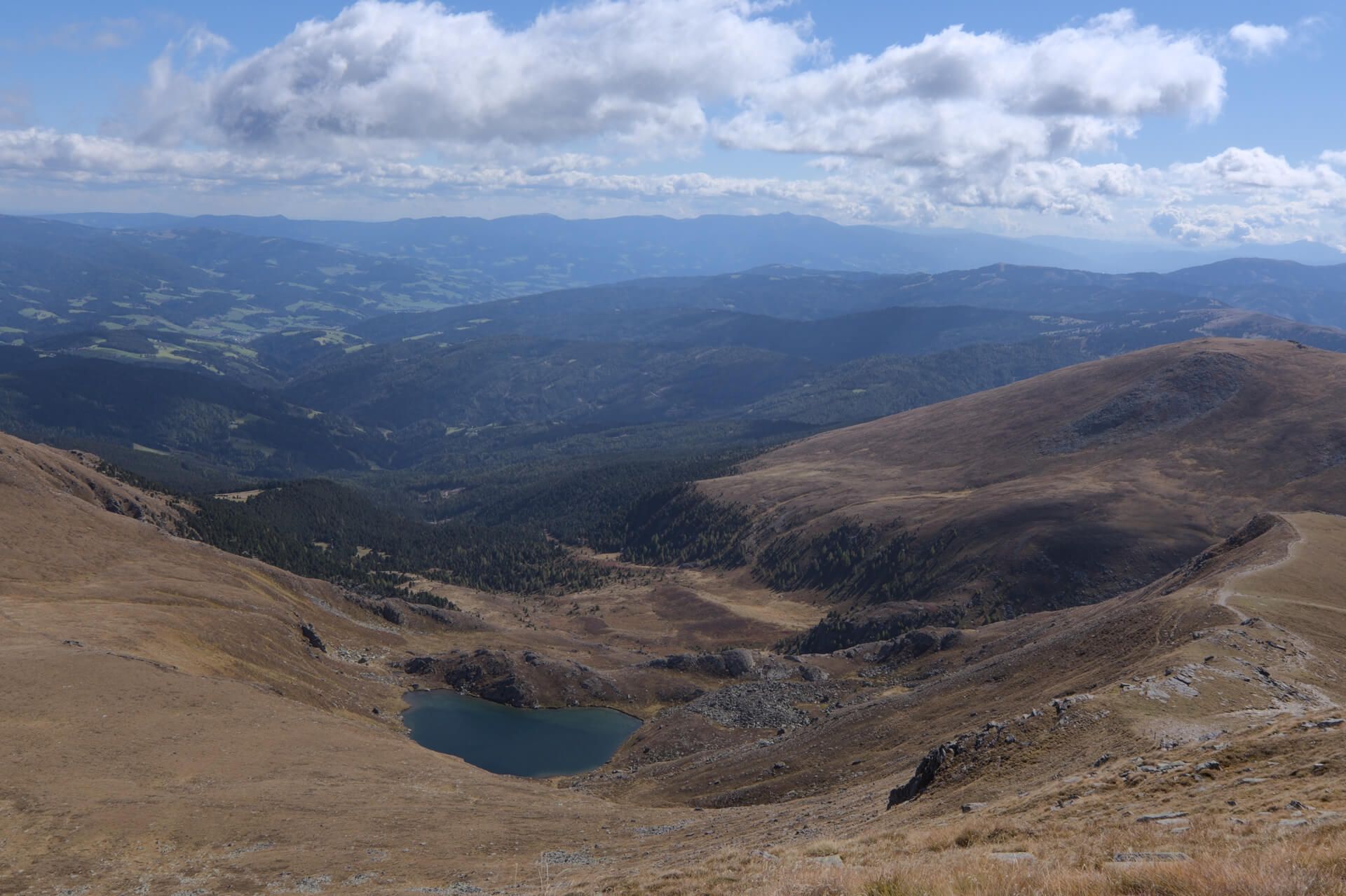 Blick von oben auf einen kleinen Bergsee in herbstlicher Almlandschaft