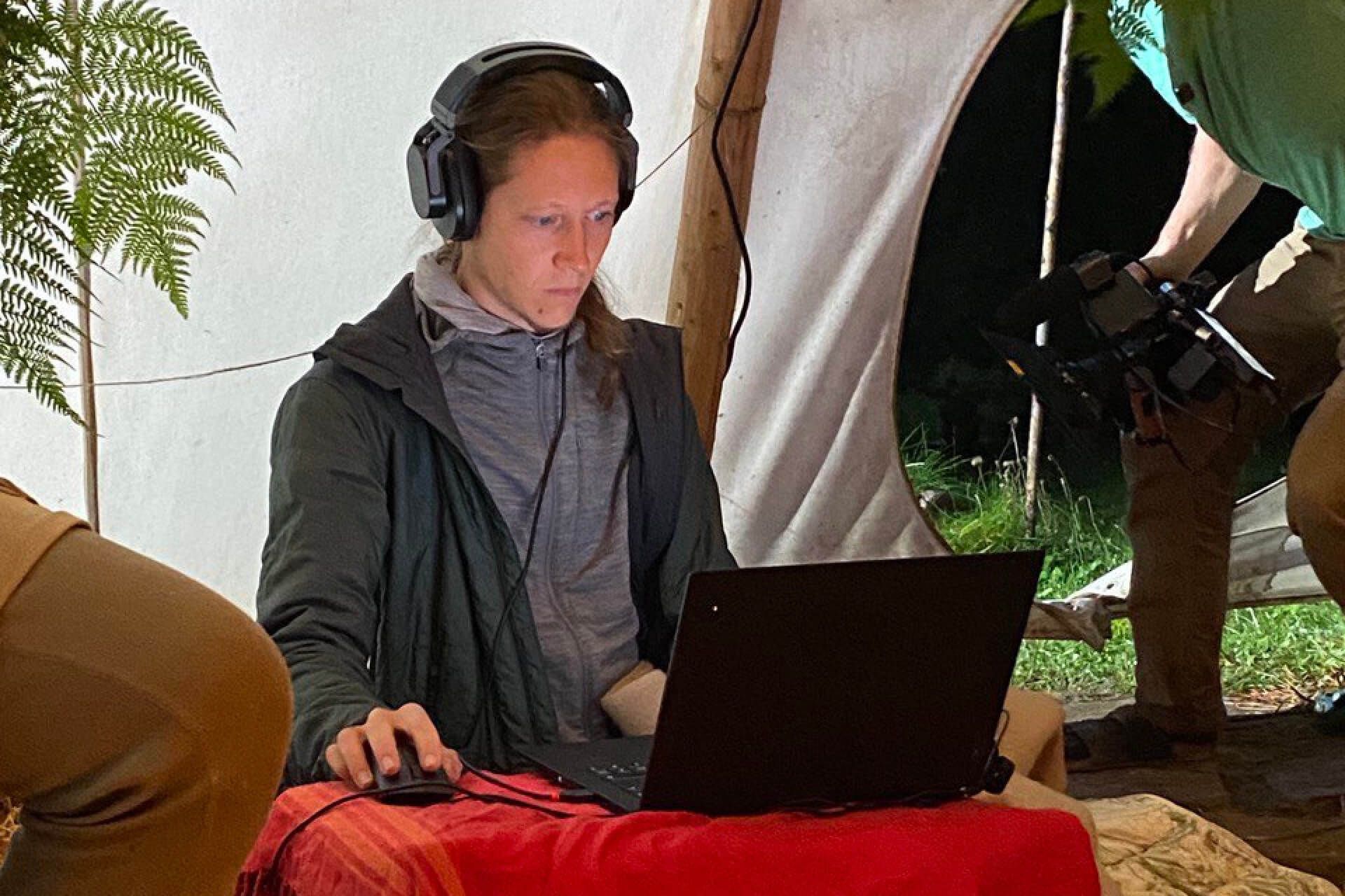 Frau mit Kopfhörern bei der Tonaufnahme am Laptop im Tipi
