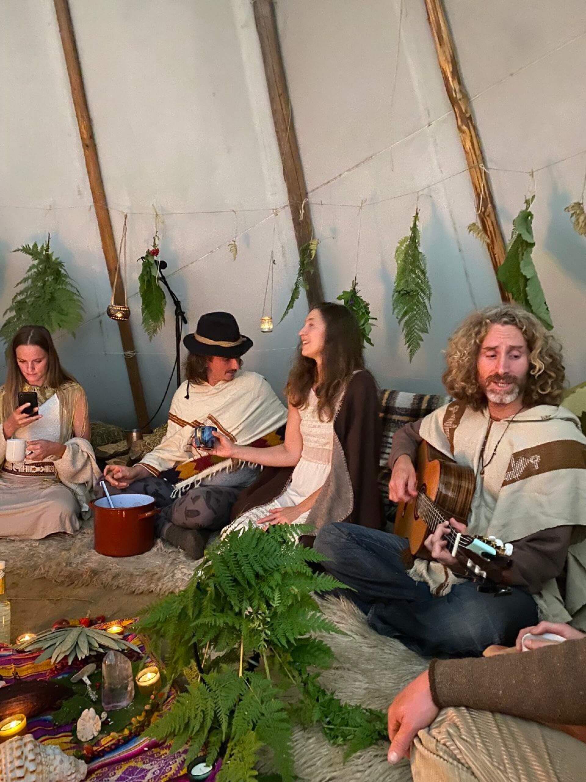 Gruppe singt und spielt Gitarre zwischen Farnen und Kerzen im Tipi
